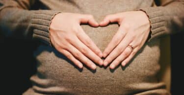 Mulher grávida com as mãos formando um coração na barriga