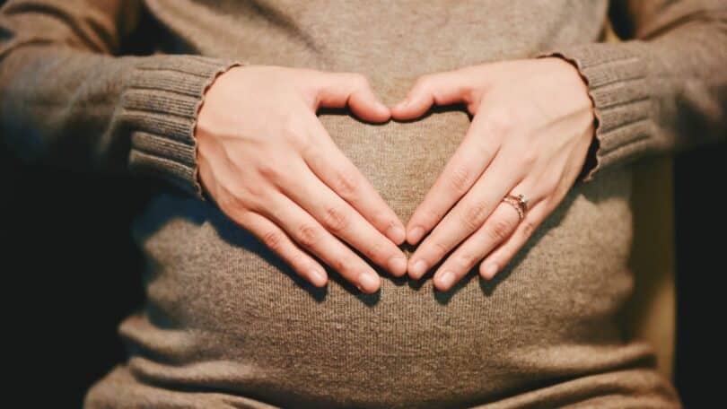 Mulher grávida com as mãos formando um coração na barriga