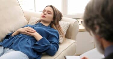 Mulher, deitada em um sofá em uma sala passando por uma consulta com um psicanalista