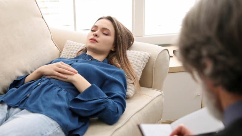Mulher, deitada em um sofá em uma sala passando por uma consulta com um psicanalista