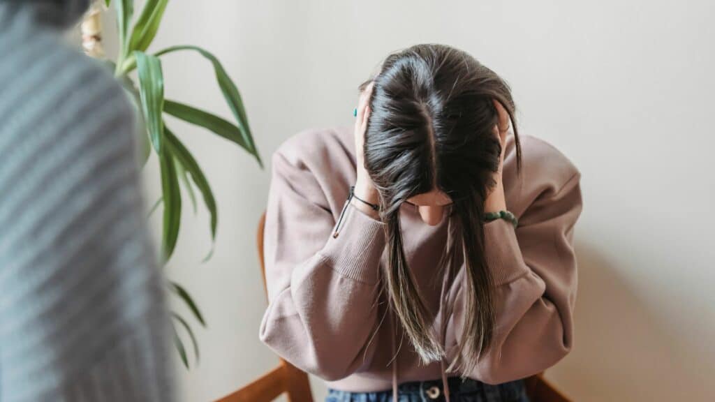 Mulher de cabeça baixa e com as mãos sobre ela, como se estivesse tapando os ouvidos