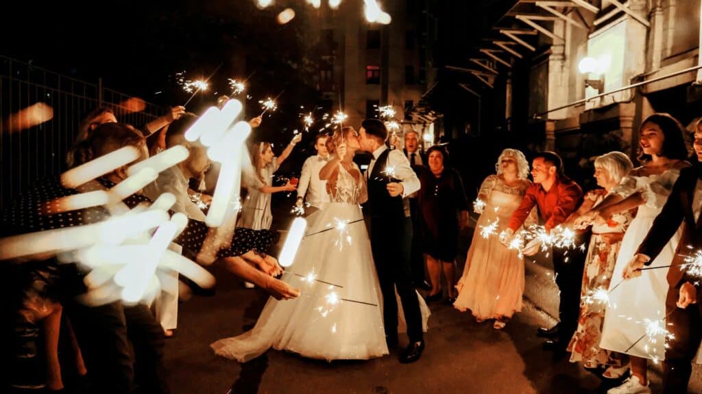 Casal de noivos se beijando enquanto os convidados estão com pavis luminosos em volta deles 