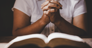 Mulher com as mãos juntas em frente à uma Bíblia. Conceito de oração