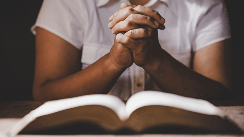 Mulher com as mãos juntas em frente à uma Bíblia. Conceito de oração