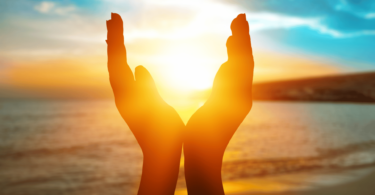 Pessoa com mãos em formato de concha na praia, vendo o pôr do sol