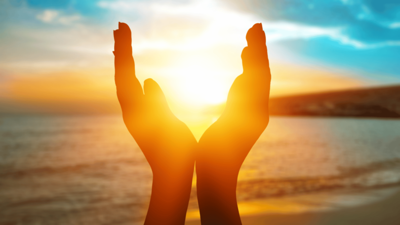 Pessoa com mãos em formato de concha na praia, vendo o pôr do sol