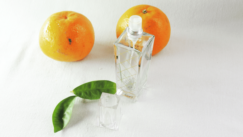 Frasco de vidro de perfume com laranjas ao lado. 