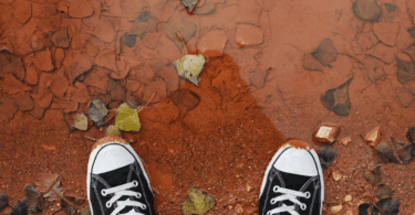 Pés calçando tênis da Converse, em lama vermelha.