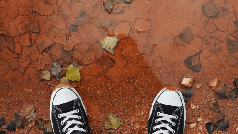 Pés calçando tênis da Converse, em lama vermelha.