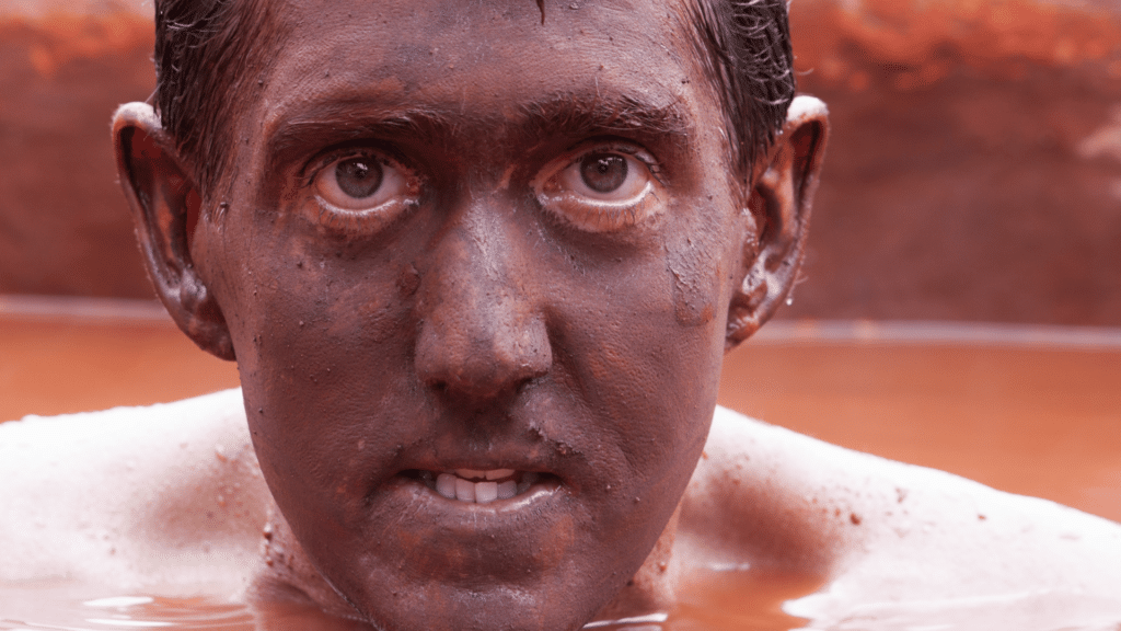 Homem com rosto sujo, dentro de lago com lama. 