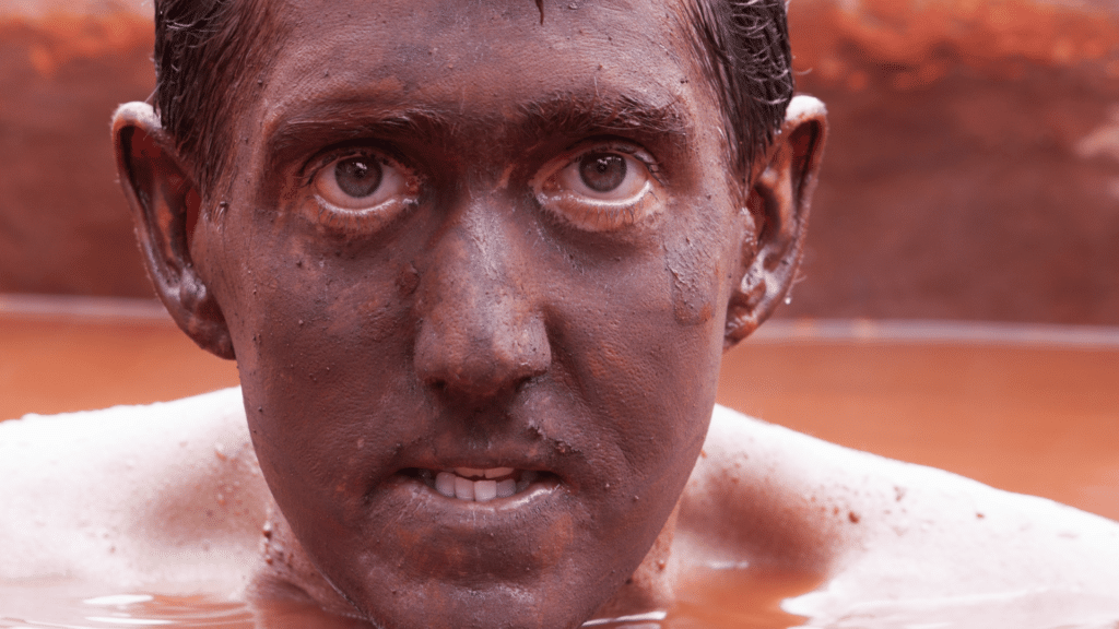 Homem com rosto sujo, dentro de lago com lama.