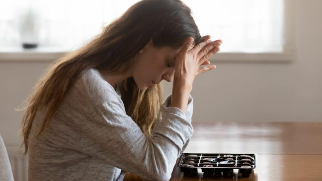 Mulher com as mãos na cabeça, e a cabeça baixa como se estivesse com ansiedade