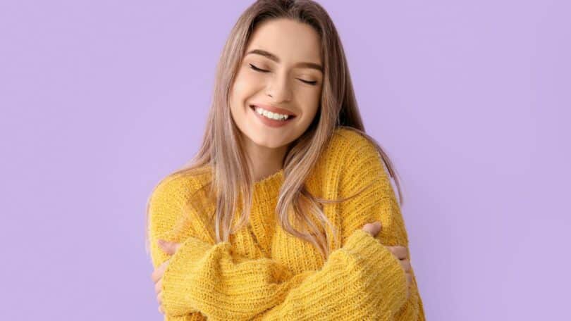 Mulher abraçando a si mesma de olhos fechados e sorrindo