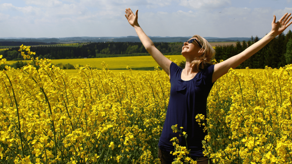 Mulher em um campo cheio d eflores, vibrando positividade. 