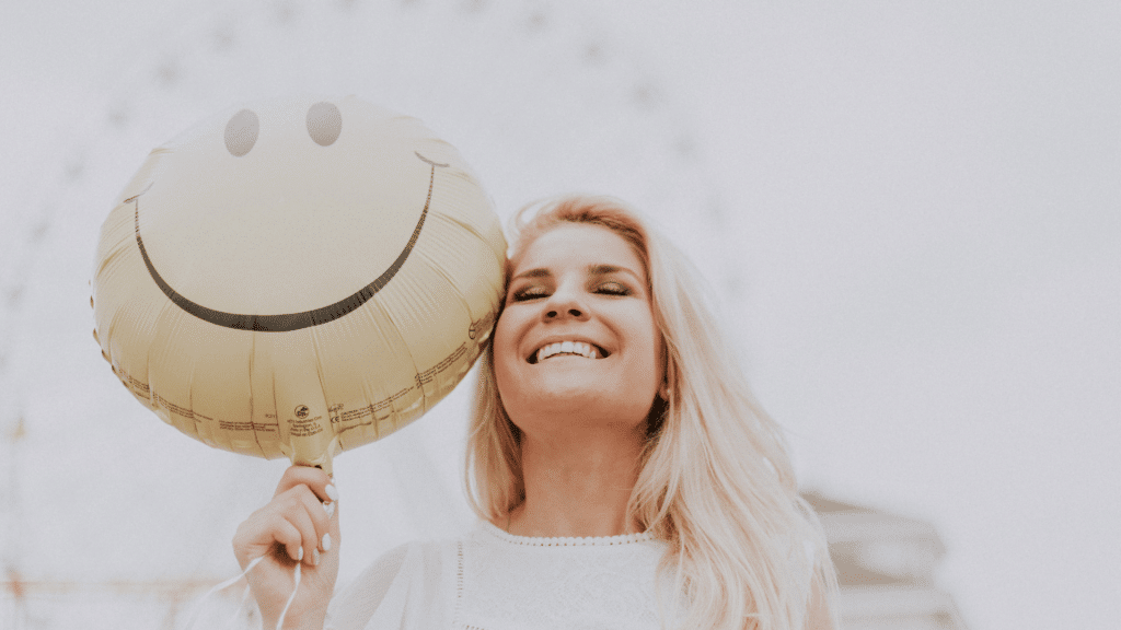Mulher sorrindo com um balão amarelo com carinha feliz na mão