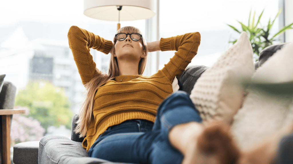 Mulher deitada em sofá, relaxando. Relaxar como forma de autocuidado e proteção de energia.