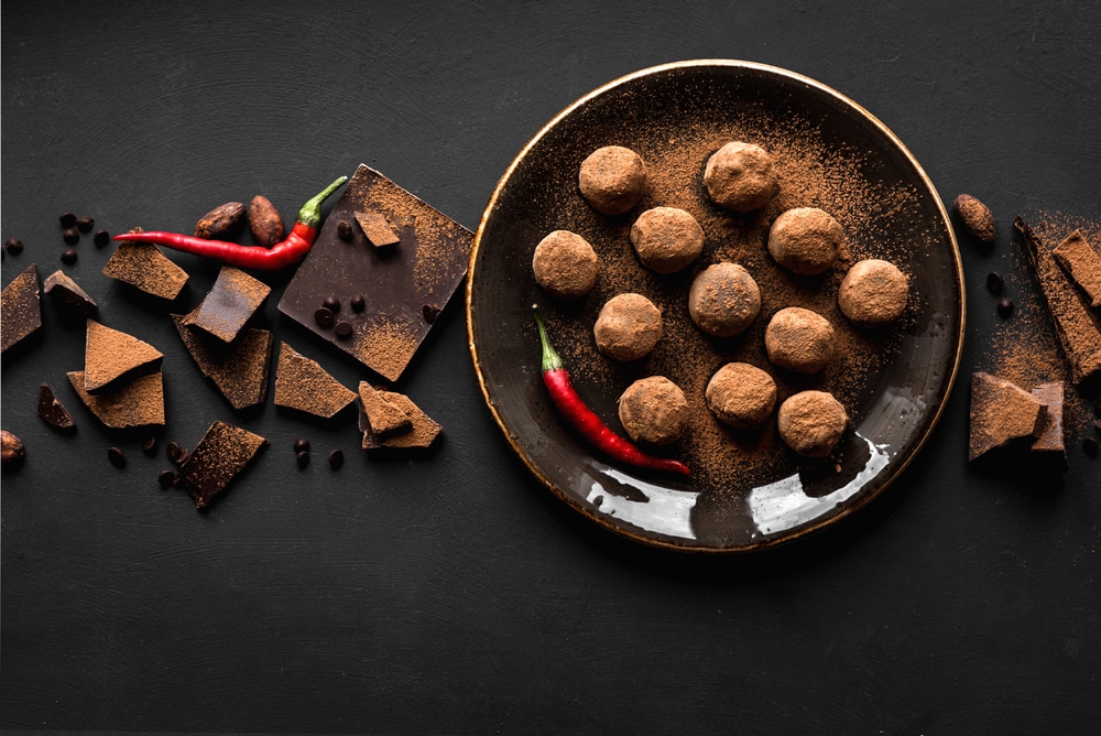 Trufas de chocolate caseiras no prato com pimenta e pedaços de chocolate, fundo preto, vista superior, espaço de cópia.