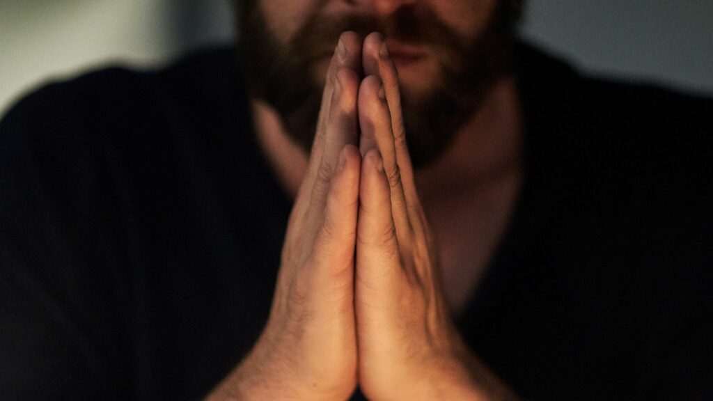 Homem com as mãos unidas como se estivesse orando