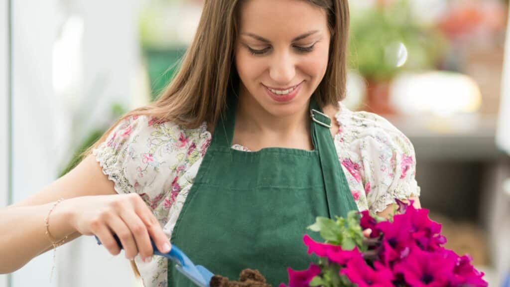 Mulher sorrindo e cultivando flores cor-de-rosa de Petúnias