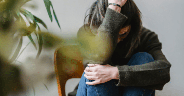 Mulher sentada no chão com as mãos na cabeça tendo uma crise de ansiedade