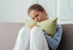 Mulher abraçando uma almofada no sofá, com os olhos fechados e chorando