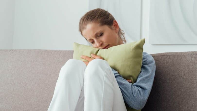 Mulher abraçando uma almofada no sofá, com os olhos fechados e chorando