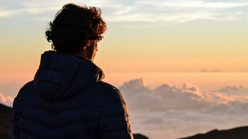Homem em cima de uma montanha contemplando o céu no pôr-do-sol