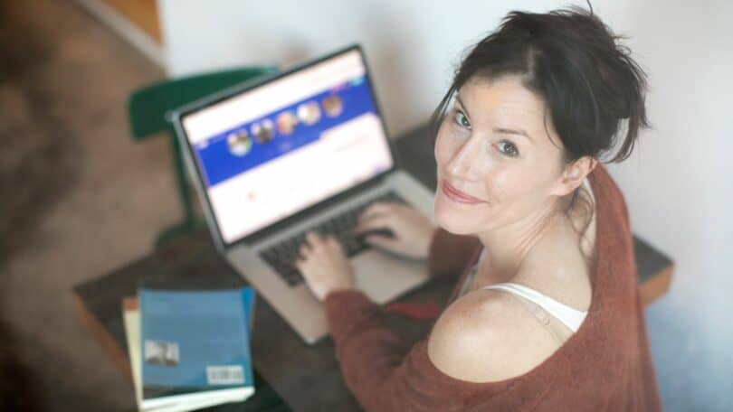 Mulher olhando para cima sorrindo, enquanto está com as mãos na tecla do notebook.