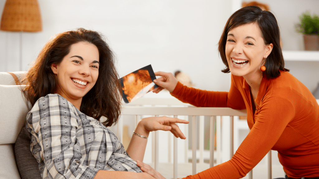 Duas mulheres sorrindo enquanto uma põe a mão na barriga da que está grávida
