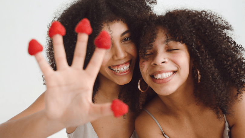 Duas irmãs sorrindo enquanto uma segura frutas com os dedos