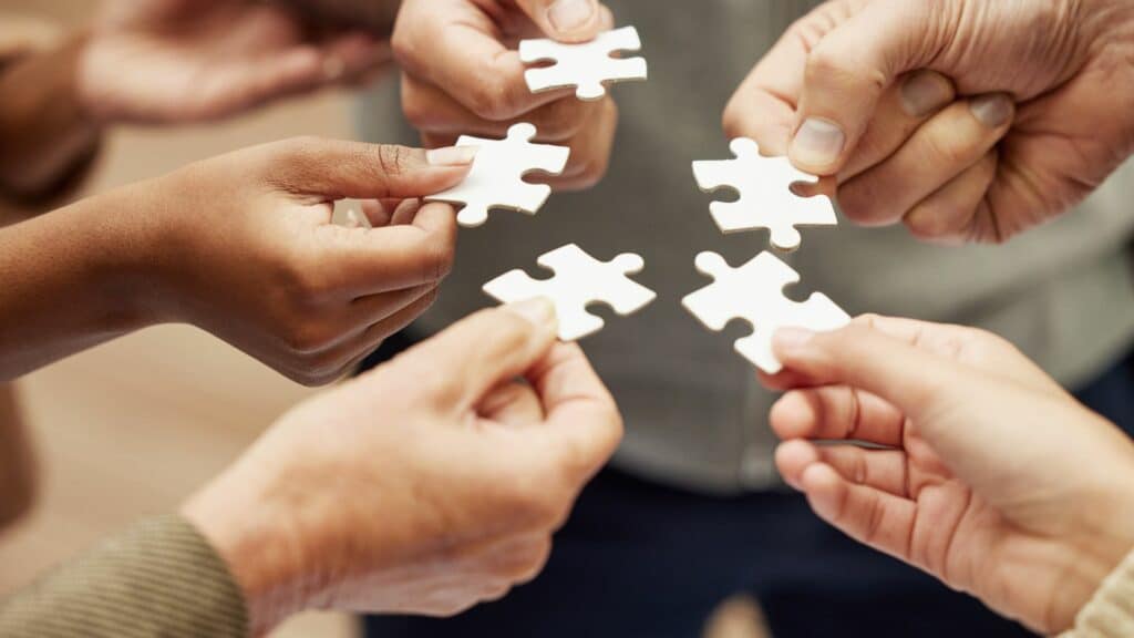 Imagem de várias mãos segurando peças de quebra-cabeça para resolver problemas.
