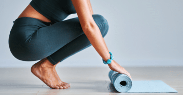 Mulher agachada no chão, abrindo tapete azul de yoga.
