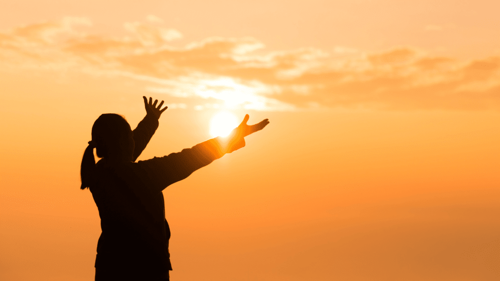 Silhueta de mulher com as mãos estendidas para o céu ao por do sol