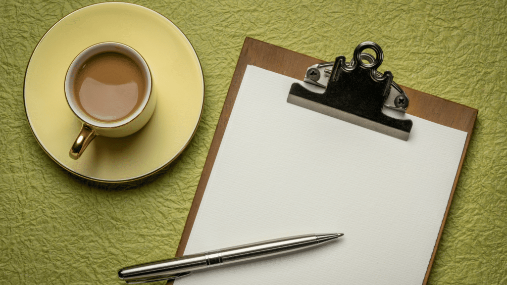 Prancheta com papel em branco e xícara de café, ao lado.