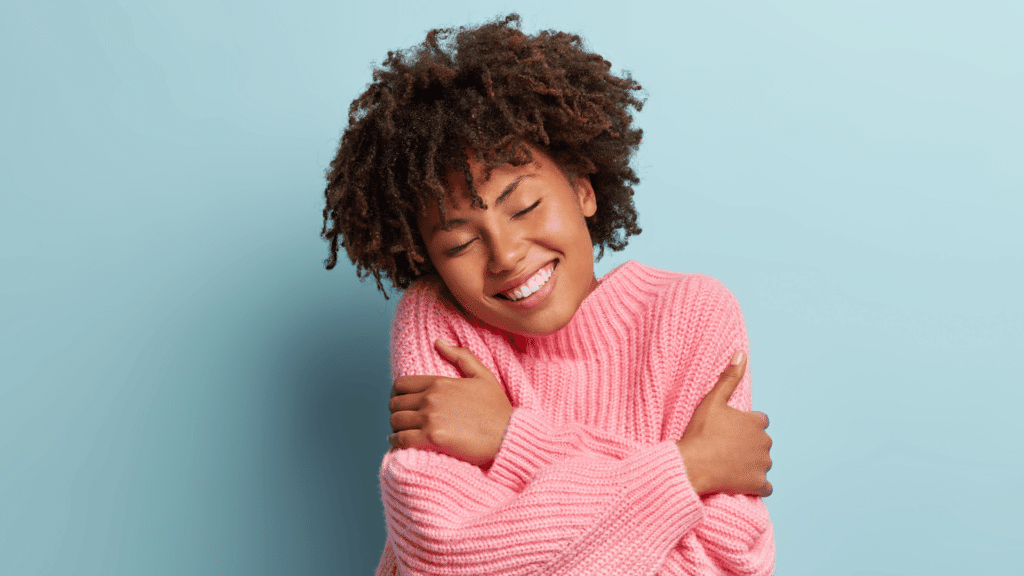 Mulher negra se abraçando de olhos fechados