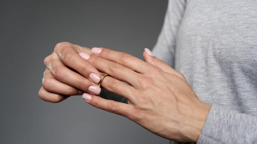 Imagem de uma mão feminina tirando a aliança de uma das mãos, indicando o fim de um relacionamento.