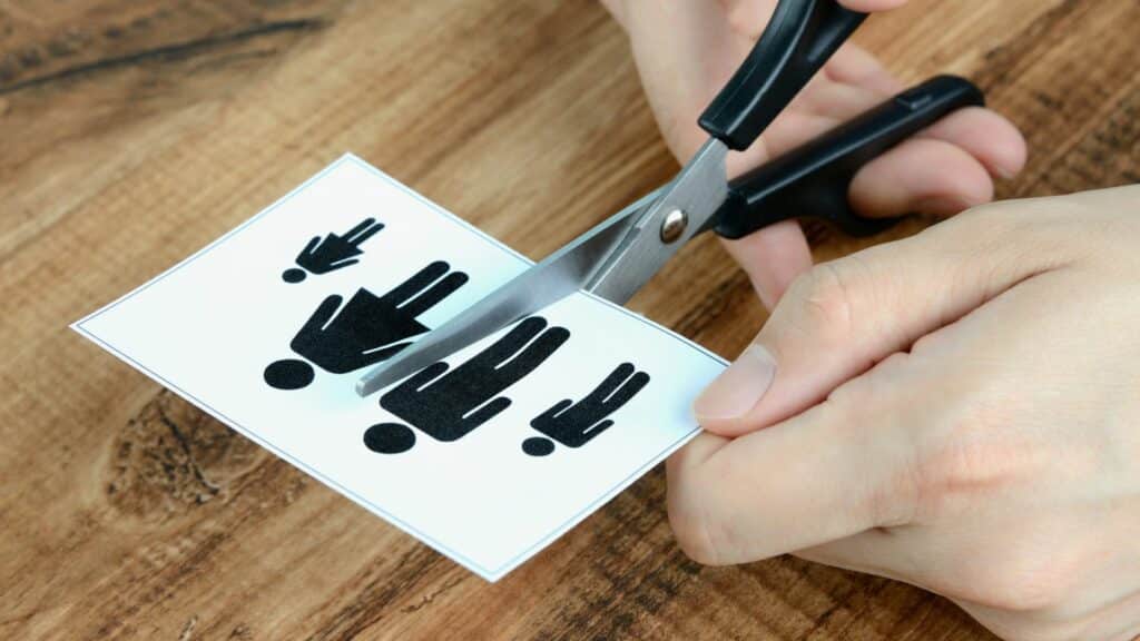 Imagem de uma mesa de madeira e sobre ela a imagem de uma ilustração familiar (pais e filhos), sendo recortada por uma mão.