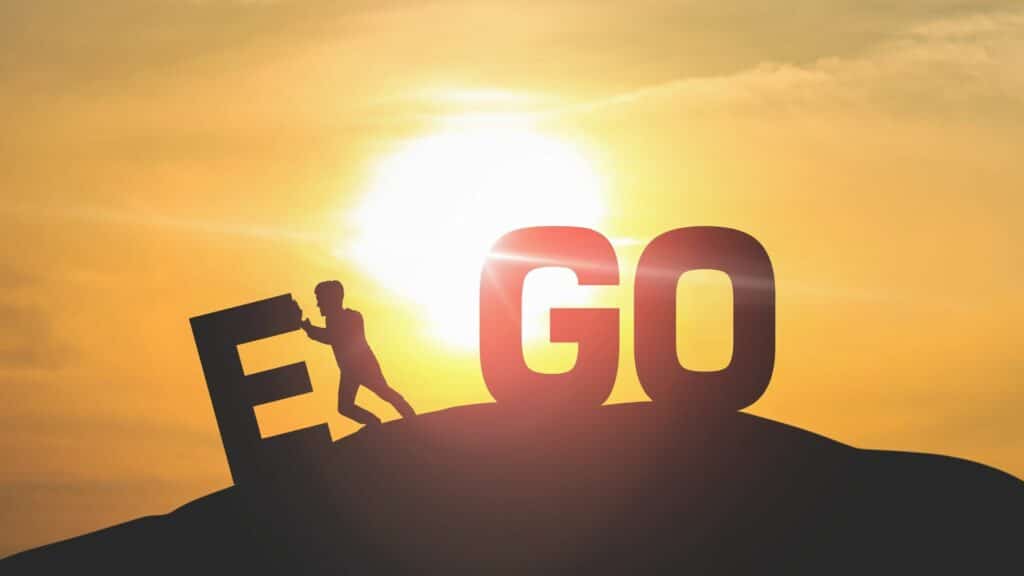 Imagem do Sol sobre uma montanha. Nela está escrito a palavra EGO e entre as letras E e G, está uma pessoa empurrando a letra E.