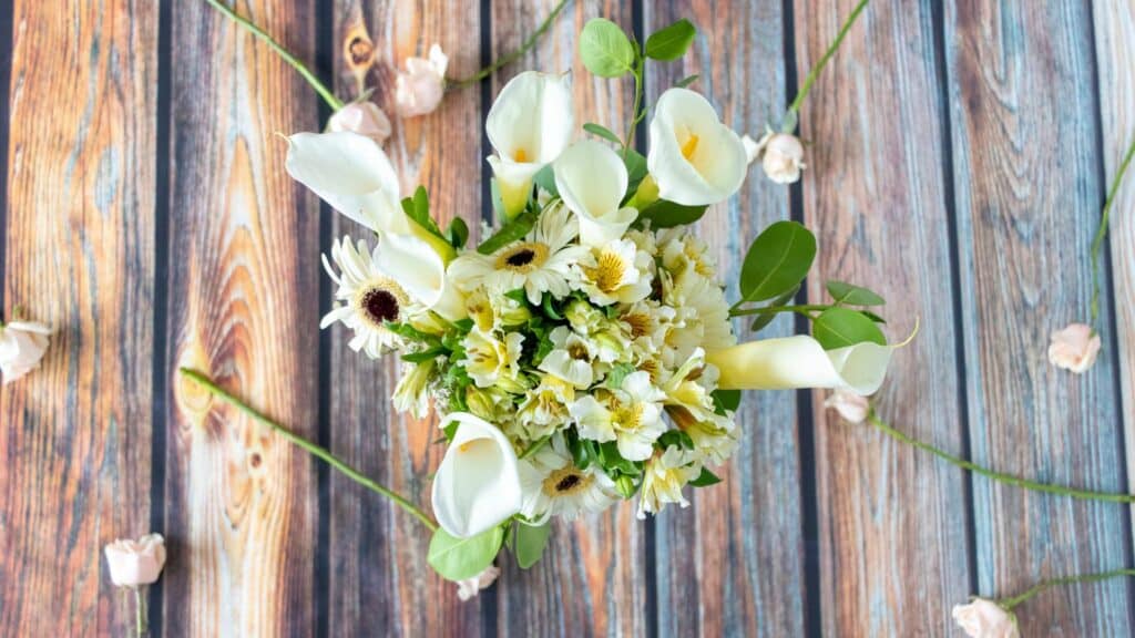 Imagem de um lindo arranjo de flor Calla sobre um piso de madeira rústica.