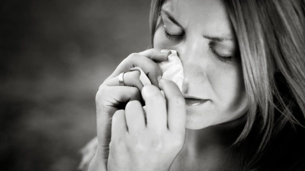 Imagem de fundo preto e em destaque uma mulher chorando e secando suas lágrimas com um lenço de papel.