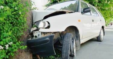 Imagem de um carro branco batido em uma árvore.