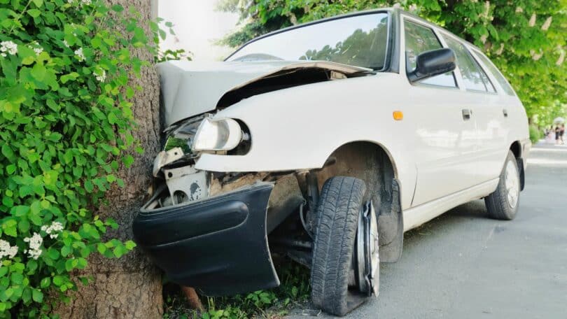 Imagem de um carro branco batido em uma árvore.