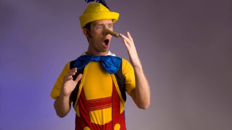 Imagem de um homem fantasiado de Pinóquio olhando para o seu nariz que cresceu devido a mentira que ele contou.