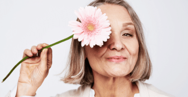 Mulher idosa segurando flor no rosto. Conceito de menopausa.