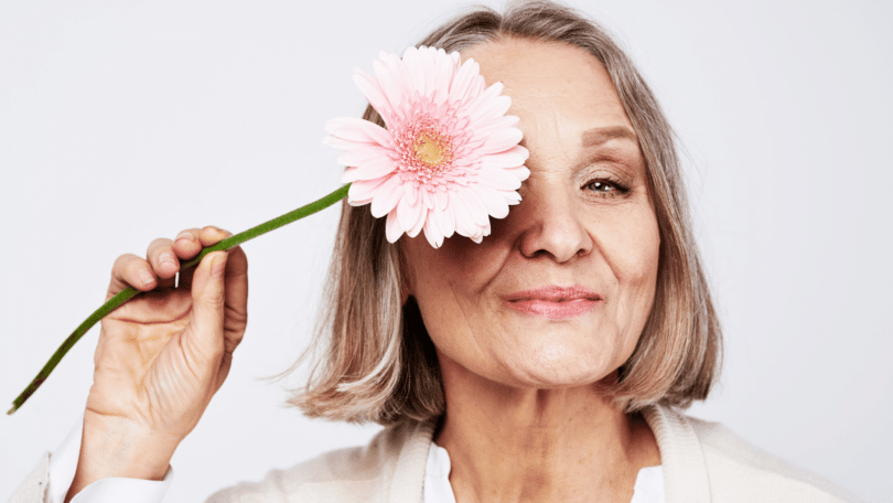 Mulher idosa segurando flor no rosto. Conceito de menopausa.