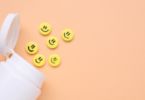 Garrafa e pílulas antidepressivas amarelas com rostos felizes em fundo laranja pálido.