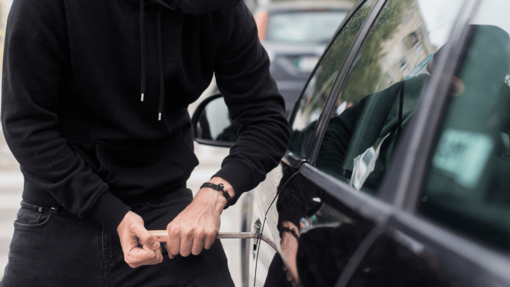 Homem encapuzado tentando roubar carro, em espaço público.