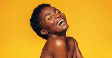 Mulher negra sentindo-se feliz, enquanto sorri. Ela está sobre um fundo amarelo ouro.
