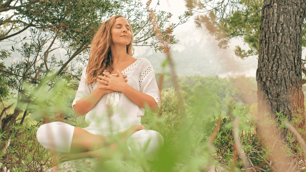 Mulher meditando com as mãos no peito, em uma floresta.