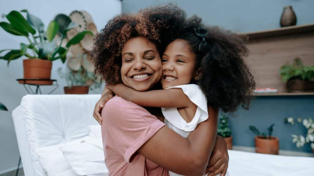 Mãe e filha se abraçando enquanto as duas sorriem, durante a comemoração do Dia das Mães. 